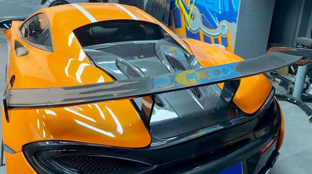 Orange sports car with a large rear wing in a showroom setting